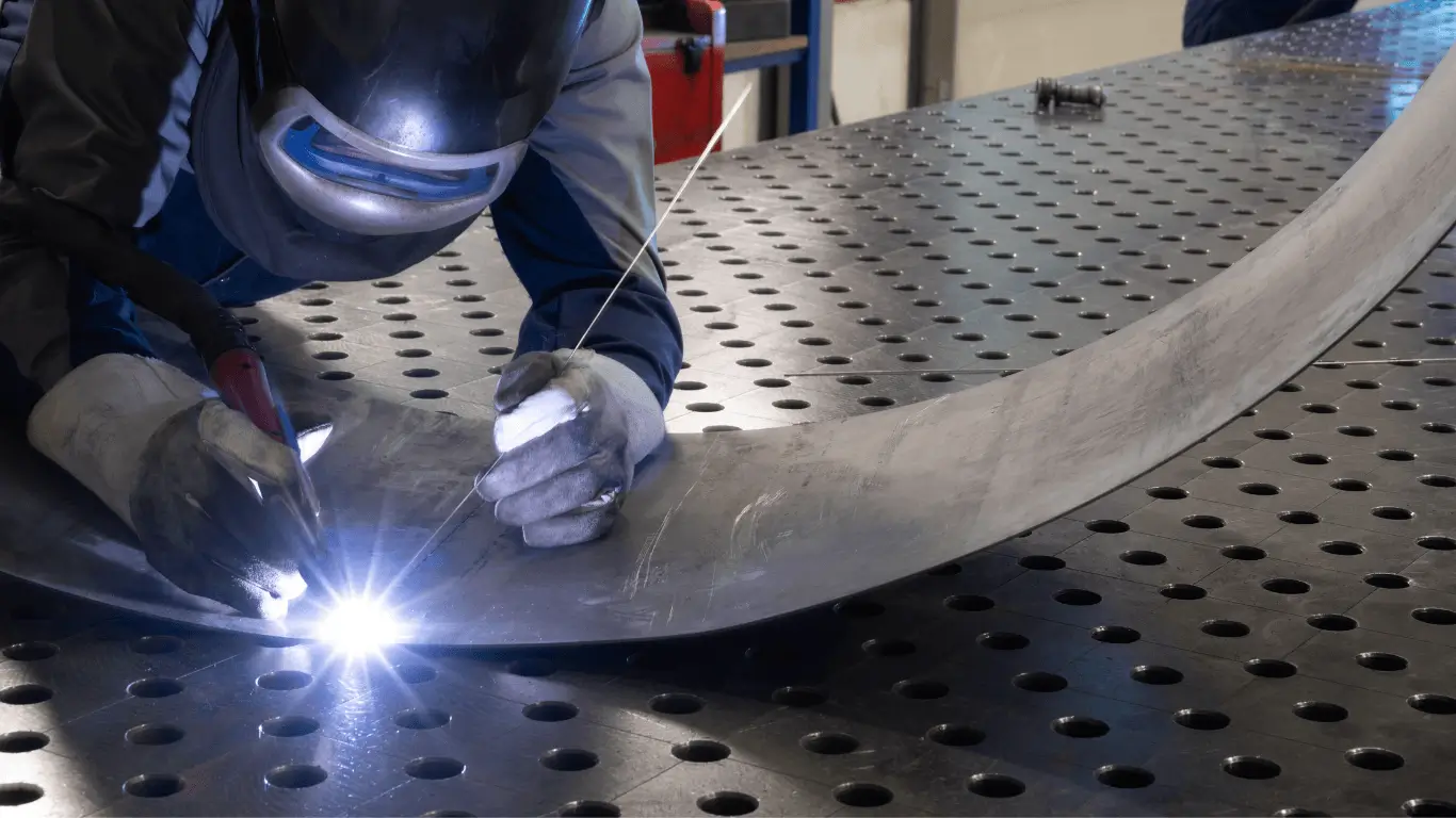 Welder fabricating a curved metal component on a precision welding table<br />
